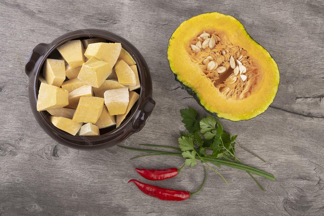 Vista superior de pedaços de kabocha em uma tigela com meia fruta, pimenta e