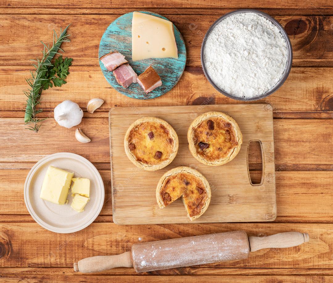 Quiche lorraine caseiro sobre placa de madeira com ingredientes