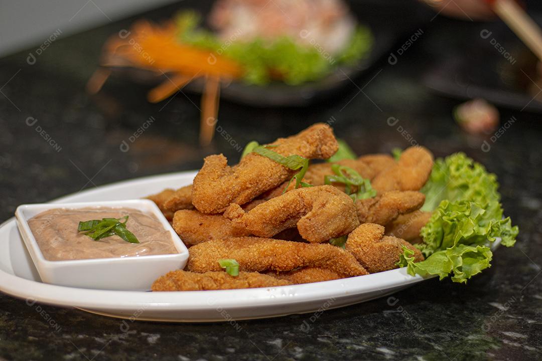 Dedo de peixe com alface em um prato branco  sobre fundo de pedra preto. Comida típica.