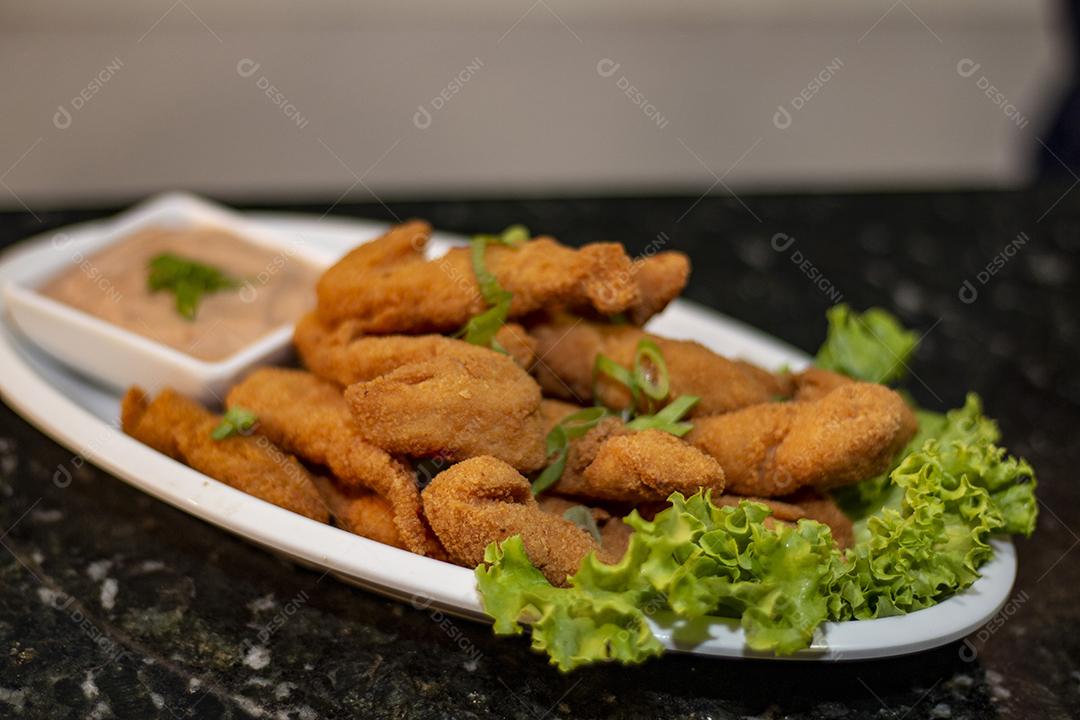 Dedo de peixe com alface em um prato branco  sobre fundo de pedra preto. Comida típica.