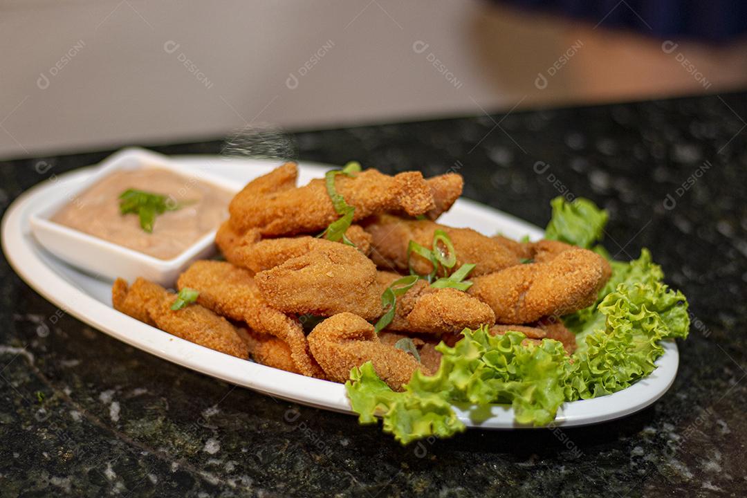 Dedo de peixe com alface em um prato branco  sobre fundo de pedra preto. Comida típica.