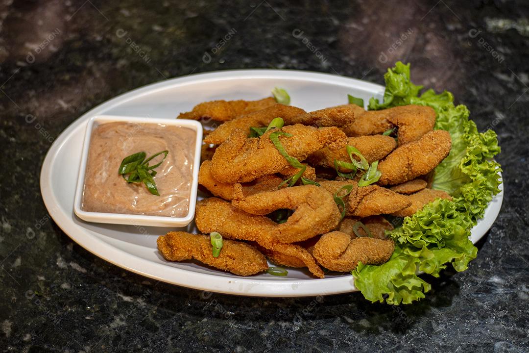 Dedo de peixe com alface em um prato branco  sobre fundo de pedra preto. Comida típica.