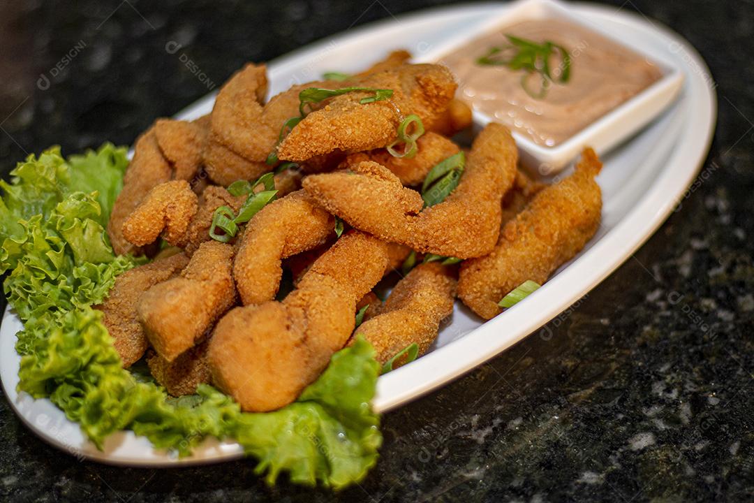 Dedo de peixe com alface em um prato branco  sobre fundo de pedra preto. Comida típica.