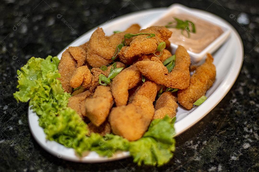 Dedo de peixe com alface em um prato branco  sobre fundo de pedra preto. Comida típica.