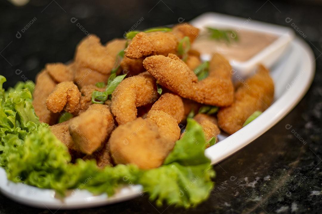 Dedo de peixe com alface em um prato branco  sobre fundo de pedra preto. Comida típica.
