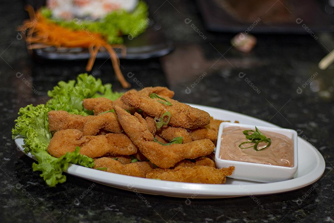 Dedo de peixe com alface em um prato branco  sobre fundo de pedra preto. Comida típica.