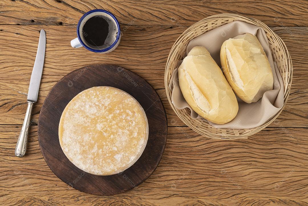 Queijo canastra artesanal de Minas Gerais, Brasil com pão e xícara de café sobre mesa de madeira.