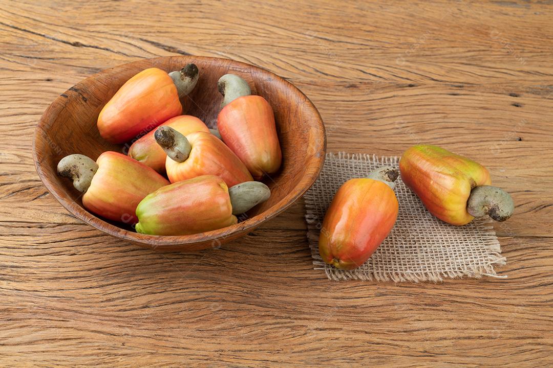 Um grupo de frutas de caju em uma tigela sobre mesa de madeira.