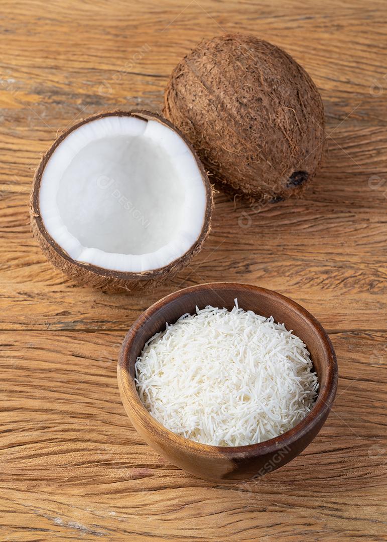Flocos de coco ralados em uma tigela com frutas sobre mesa de madeira.