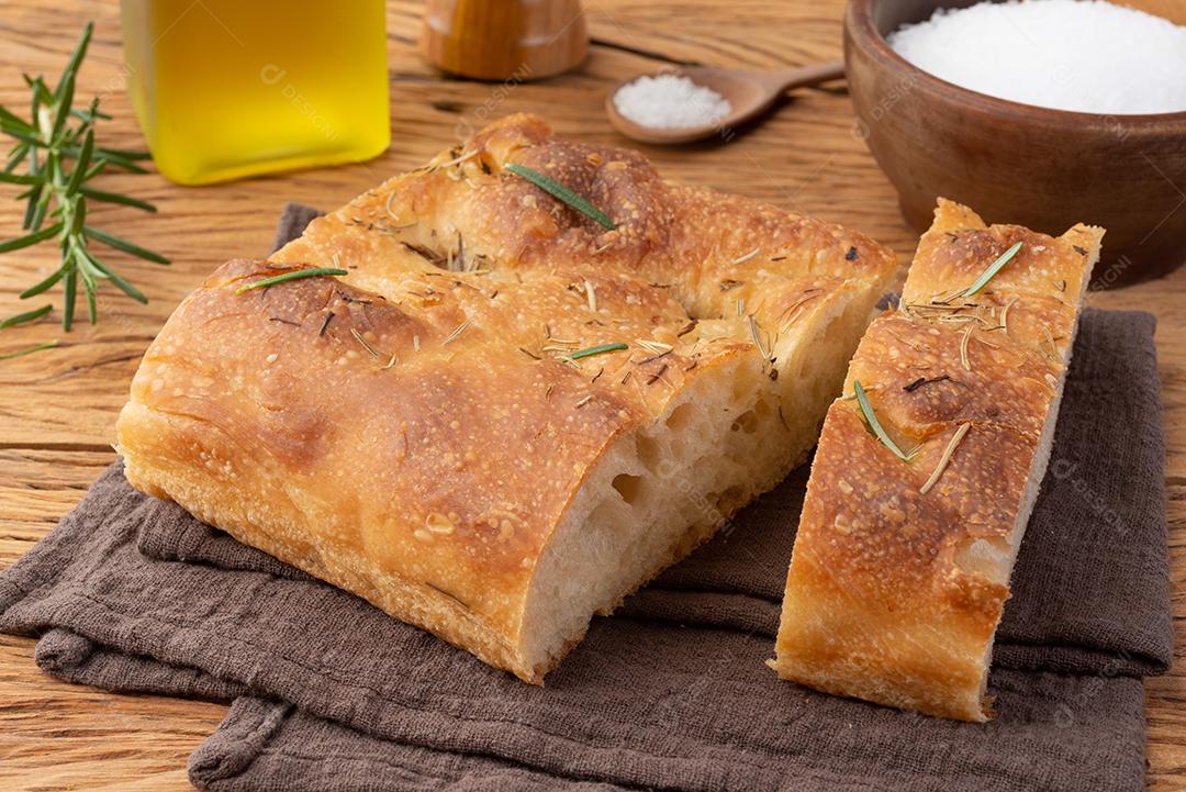 Focaccia caseira com sal, azeite e alecrim sobre mesa de madeira.