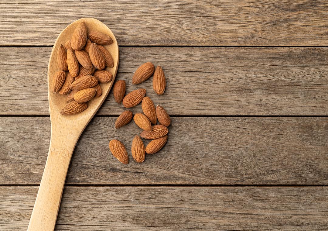 Amêndoas em uma colher sobre mesa de madeira