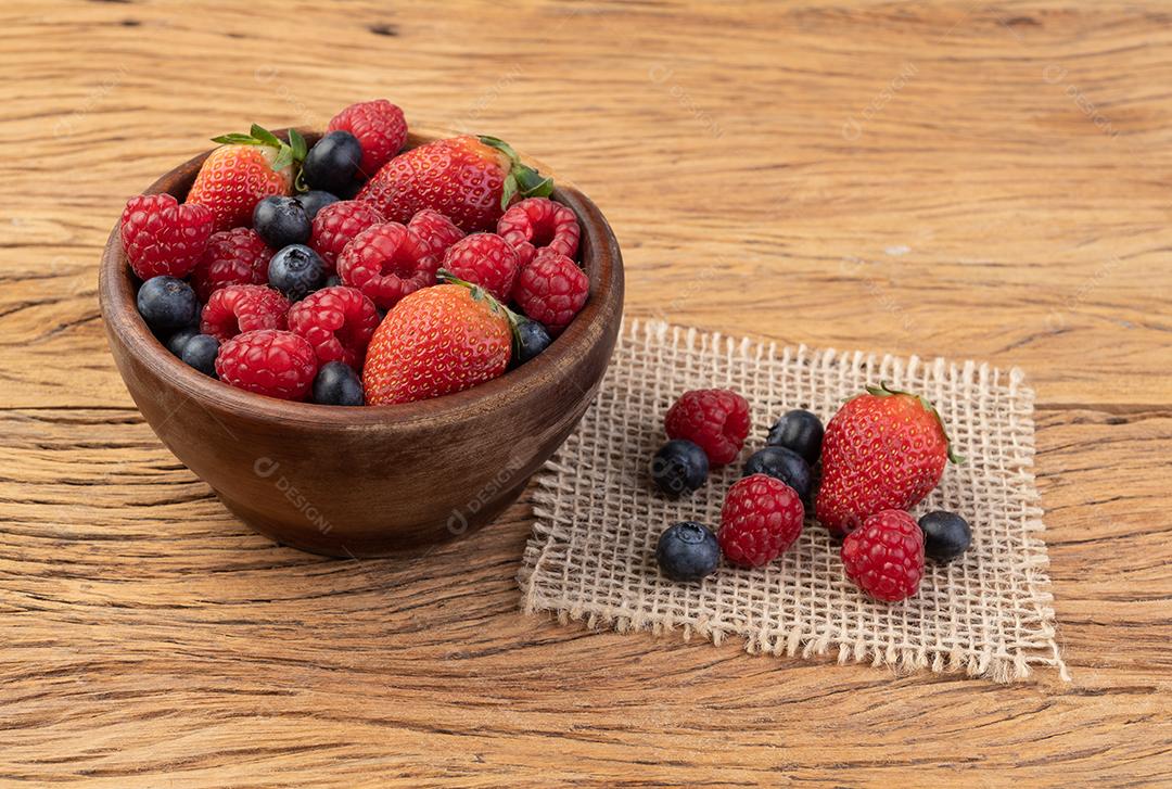 Morangos, mirtilos e framboesas em uma tigela sobre mesa de madeira.