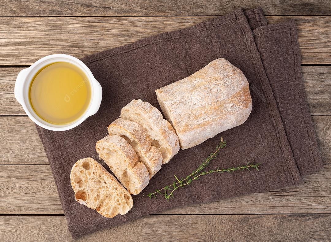 Tradicional pão ciabatta caseiro com fatias e azeite sobre mesa de madeira.