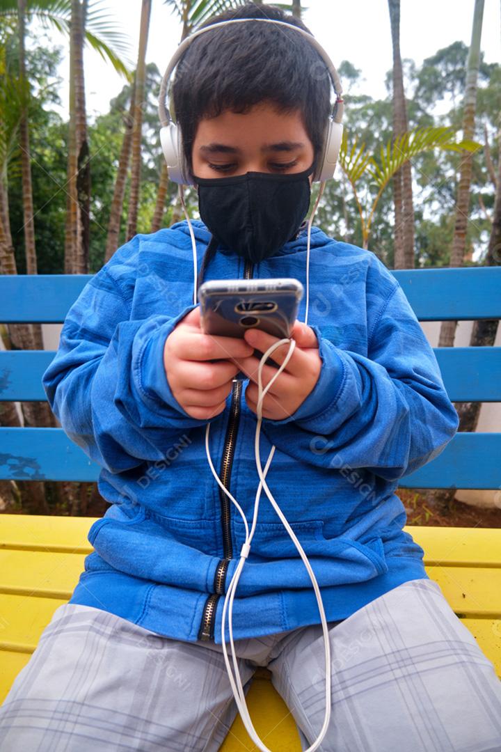 Menino brasileiro usando máscara ouvindo a música no celular