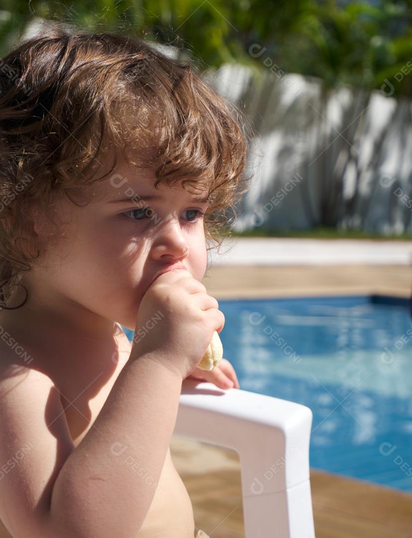 Menina comendo uma banana na piscina em um dia ensolarado