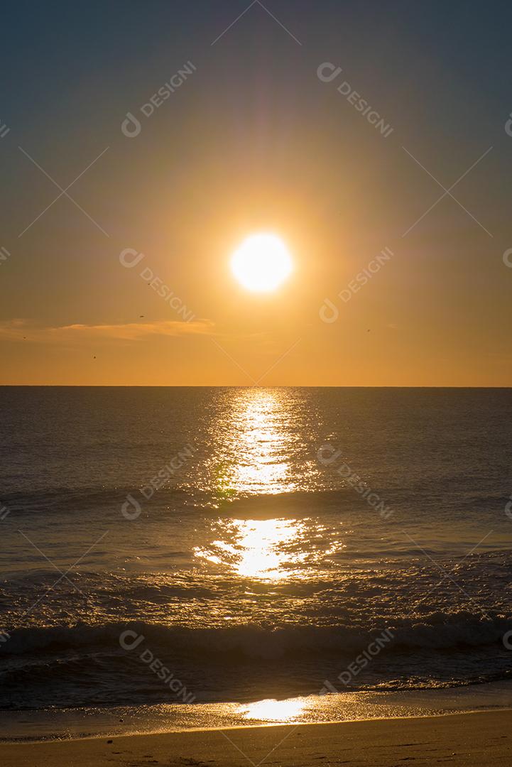 Pôr do sol na praia com sol no céu e 2 pessoas em silhueta.