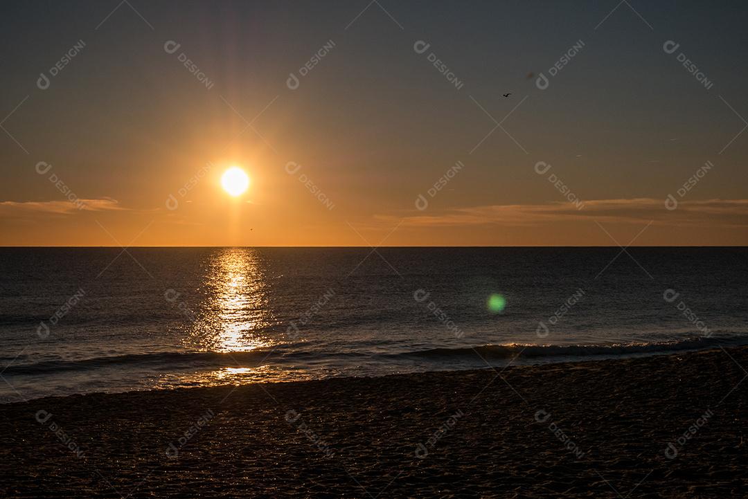 Pôr do sol na praia com sol no céu.
