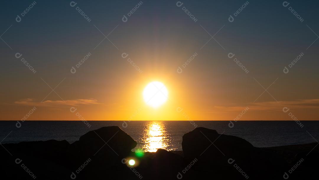 Pôr do sol na praia com sol no céu.