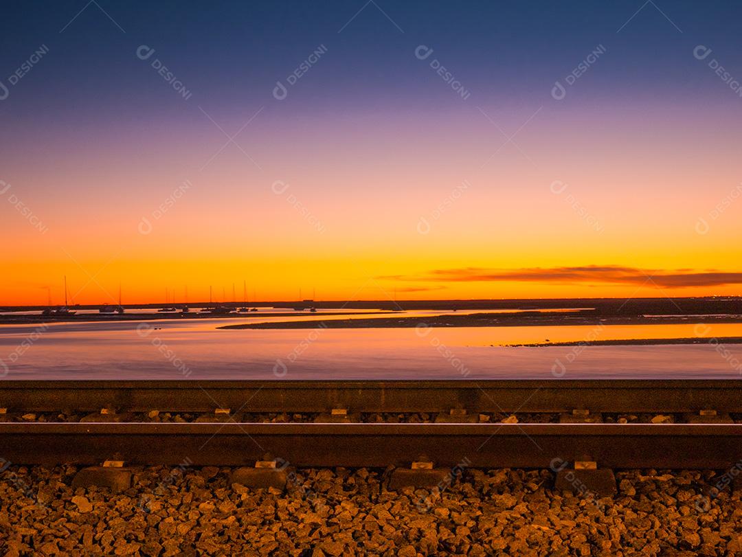 Tiro de longa exposição da estrada de ferro de Faro no pôr do sol e mar.