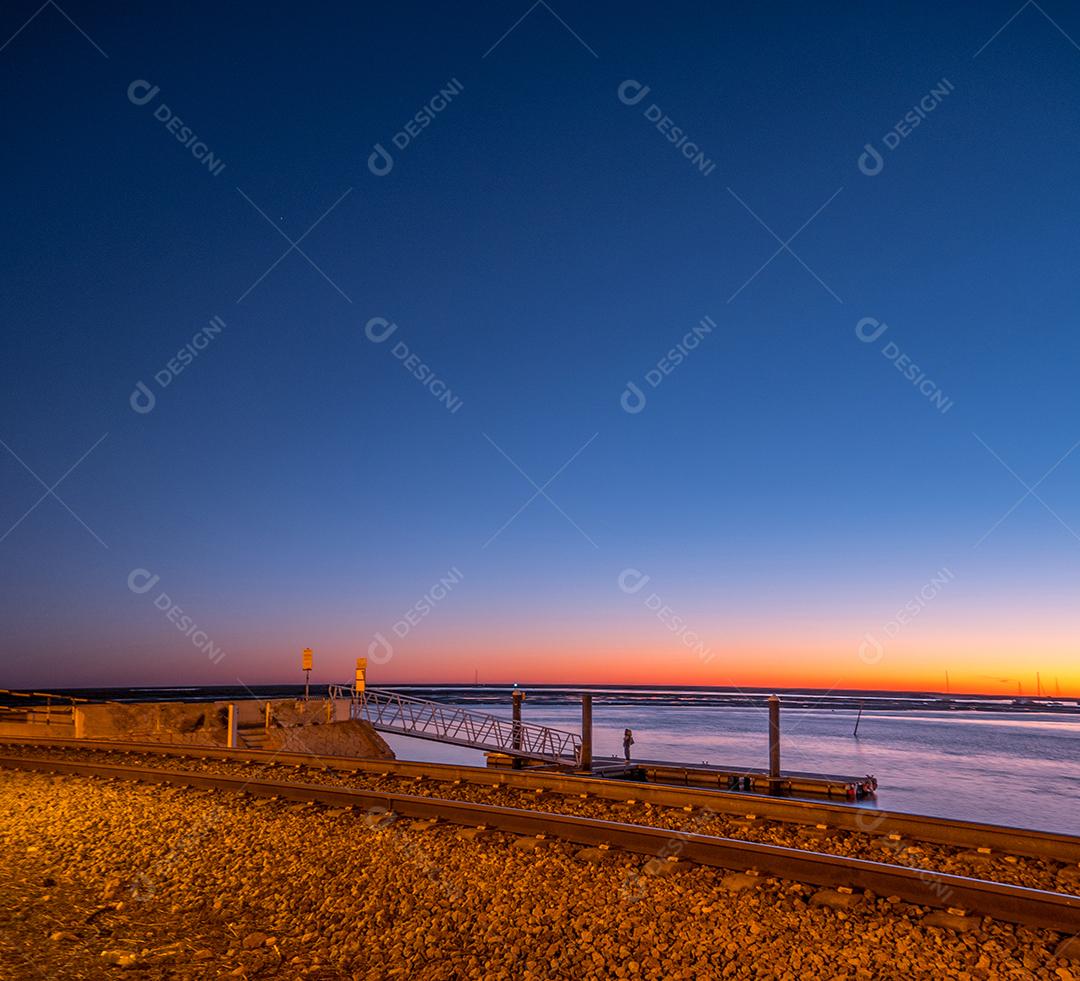 Tiro de longa exposição da estrada de ferro de Faro no pôr do sol e mar.