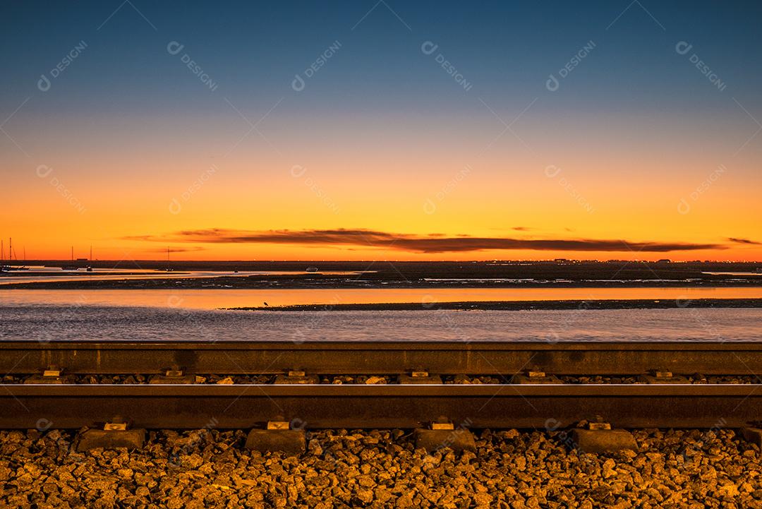 Tiro de longa exposição da estrada de ferro de Faro no pôr do sol e mar.