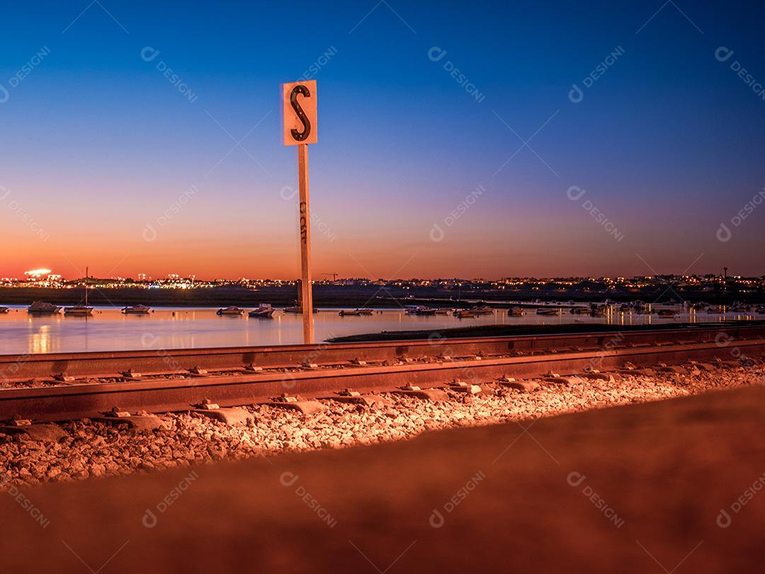 Tiro de longa exposição da estrada de ferro de Faro no pôr do sol e mar.