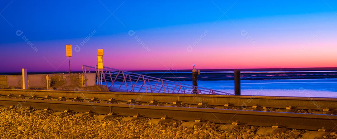 Tiro de longa exposição da estrada de ferro de Faro no pôr do sol e mar.