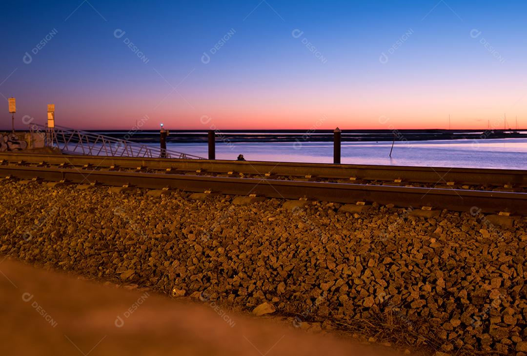 Tiro de longa exposição da estrada de ferro de Faro no pôr do sol e mar.