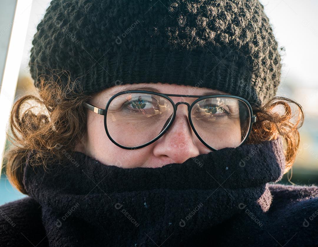 Perto de mulher com boné e óculos olhando para a câmera.