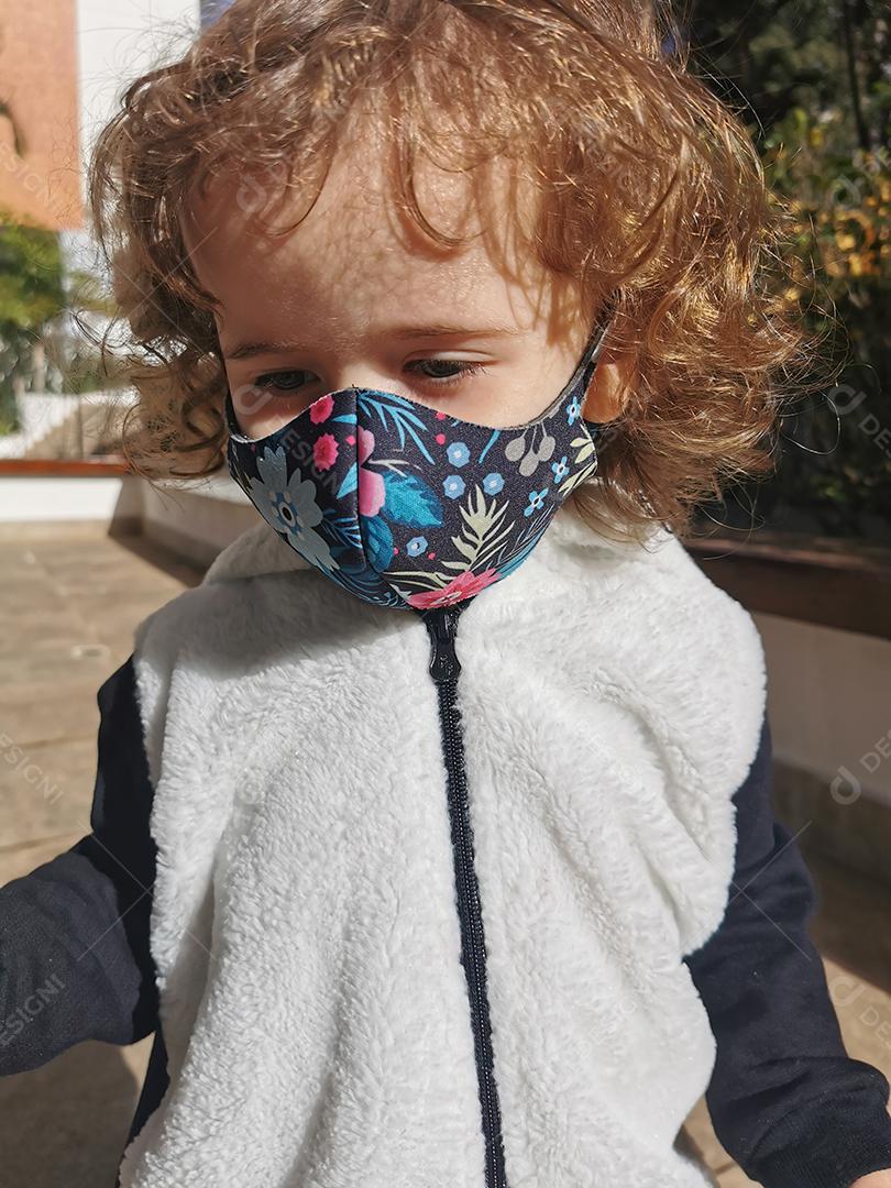 Menina brasileira sorrindo usando máscara ao ar livre.