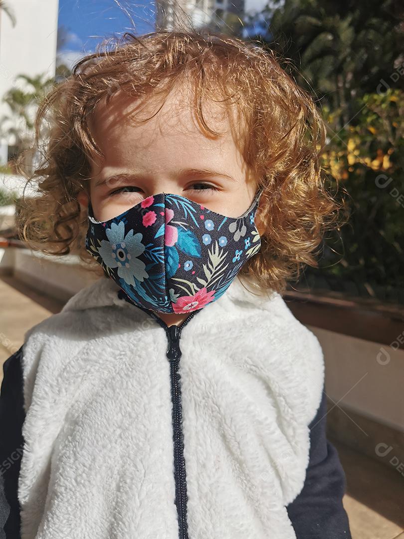Menina brasileira sorrindo usando máscara ao ar livre.