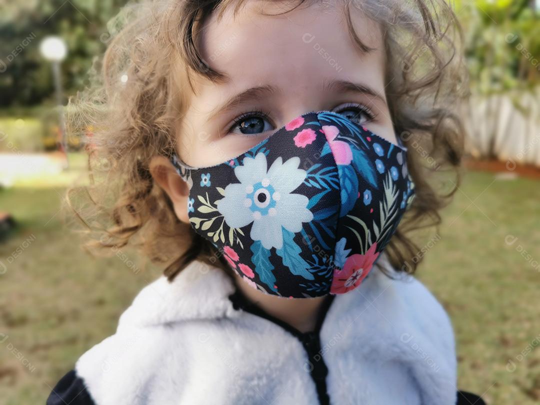Menina brasileira sorrindo usando máscara ao ar livre.