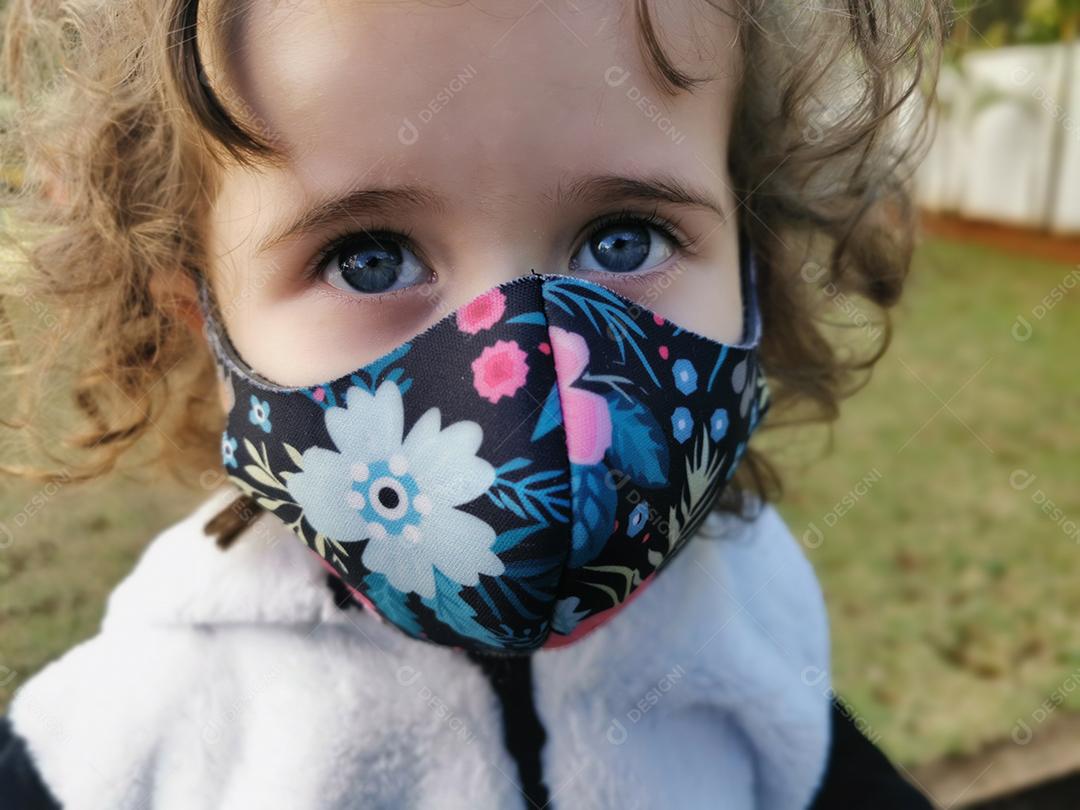 Menina brasileira sorrindo usando máscara ao ar livre.