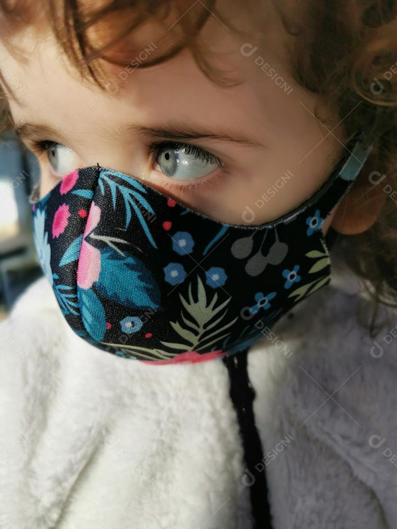 Menina brasileira olhando para o lado usando máscara ao ar livre.