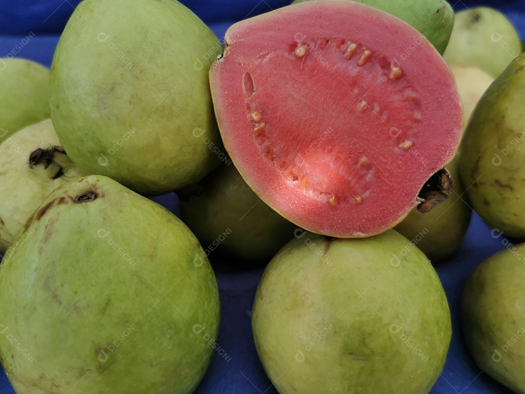 Foto de goiabas com uma delas cortada ao meio em uma feira livre.