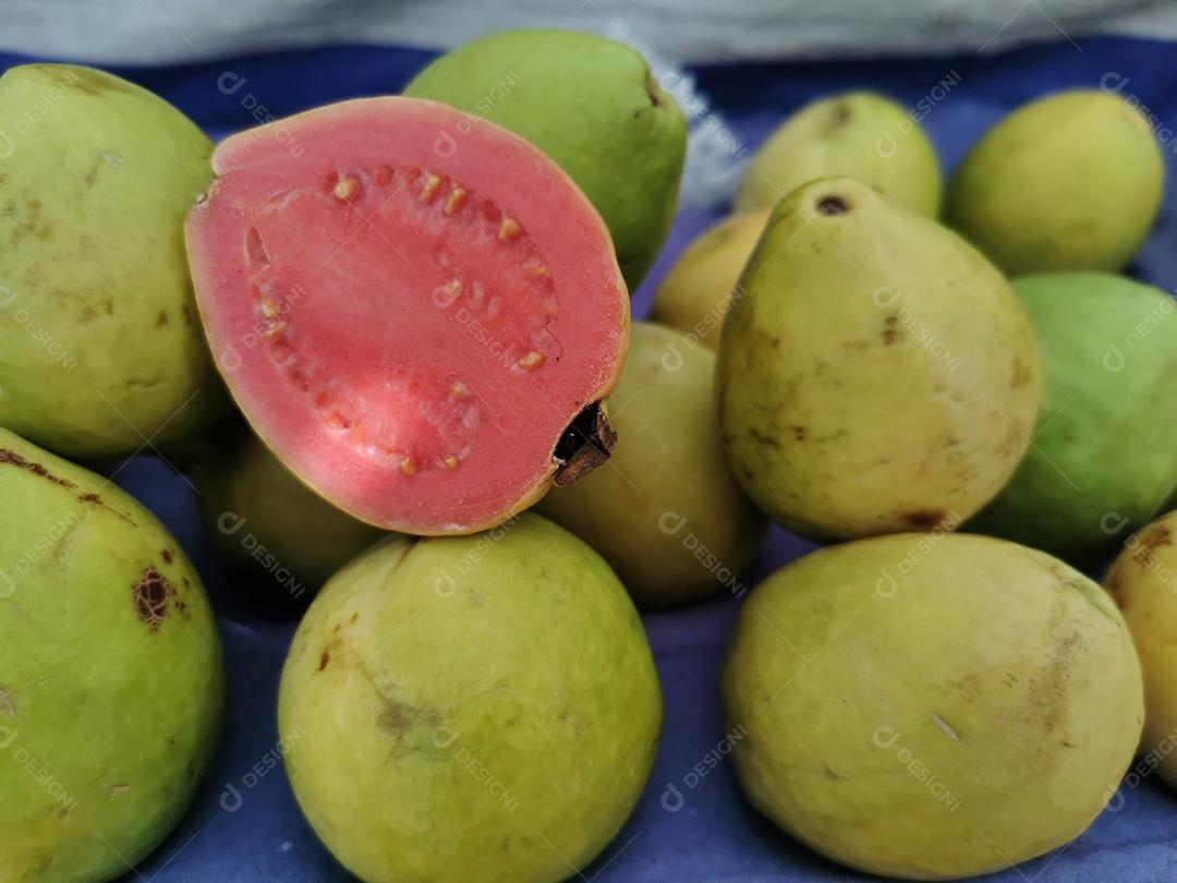 Foto de goiabas com uma delas cortada ao meio em uma feira livre.