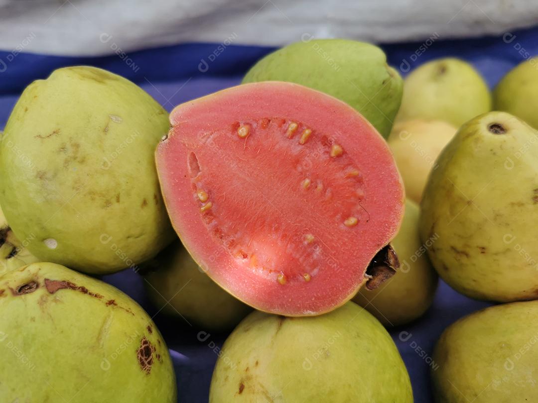 Foto de goiabas com uma delas cortada ao meio em uma feira livre.