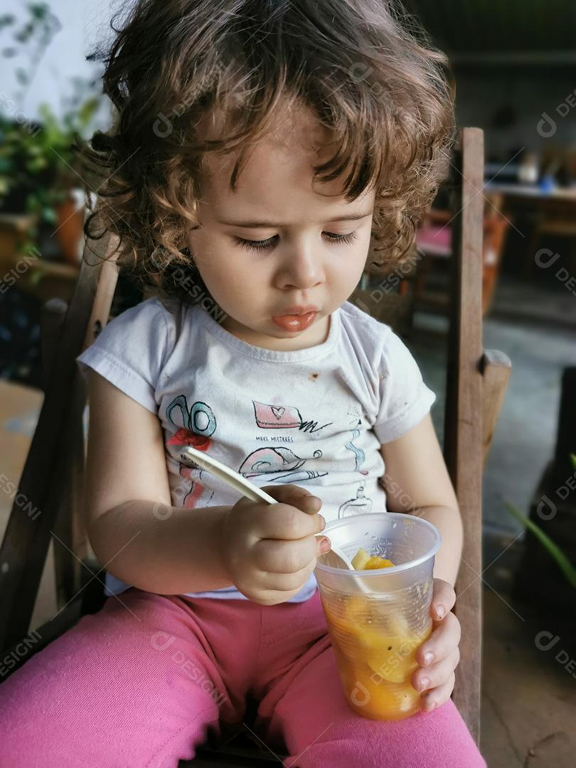 Retrato de uma garotinha comendo algumas frutas.