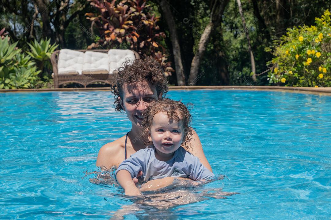 Vista de Mãe e Filha Brasileira brincando na piscina.