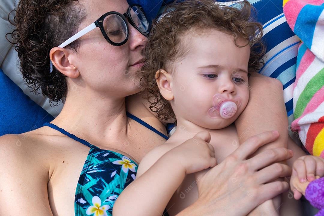 Menina usando chupeta sendo mantida por sua mãe.