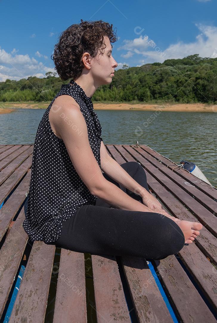 jovem meditando no píer da represa.