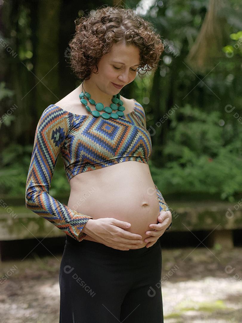 grávida jovem moderna tocando sua barriga ao ar livre.