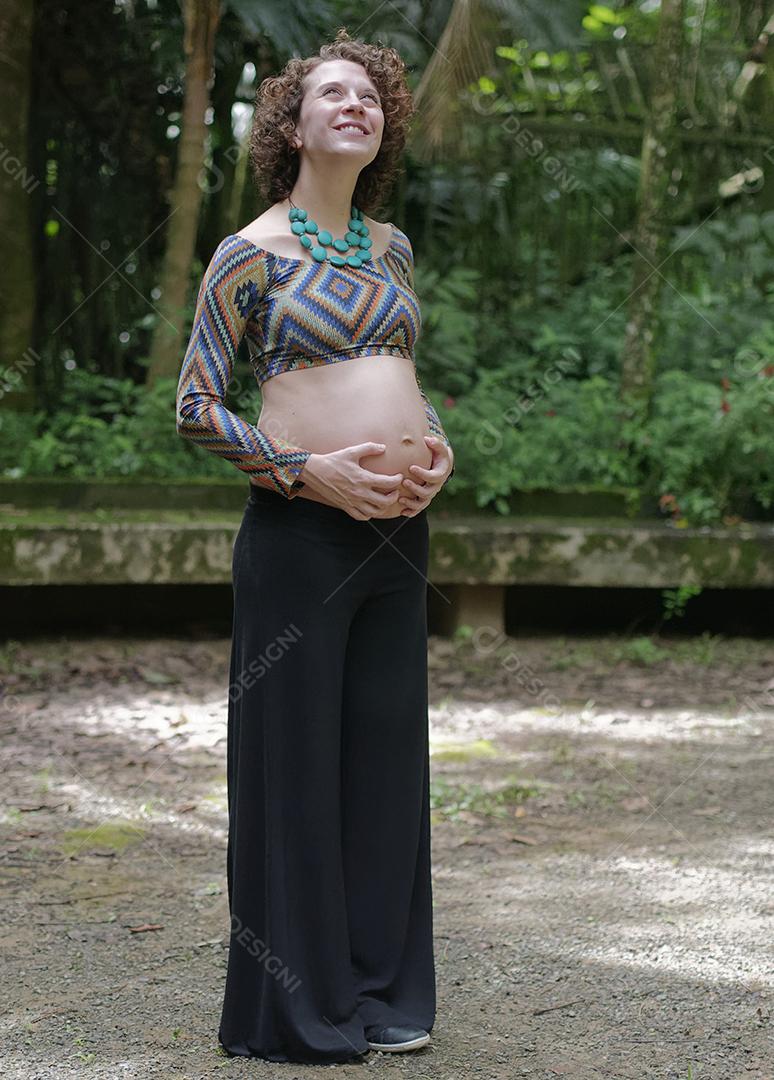 Mulher jovem moderna grávida tocando sua barriga ao ar livre.