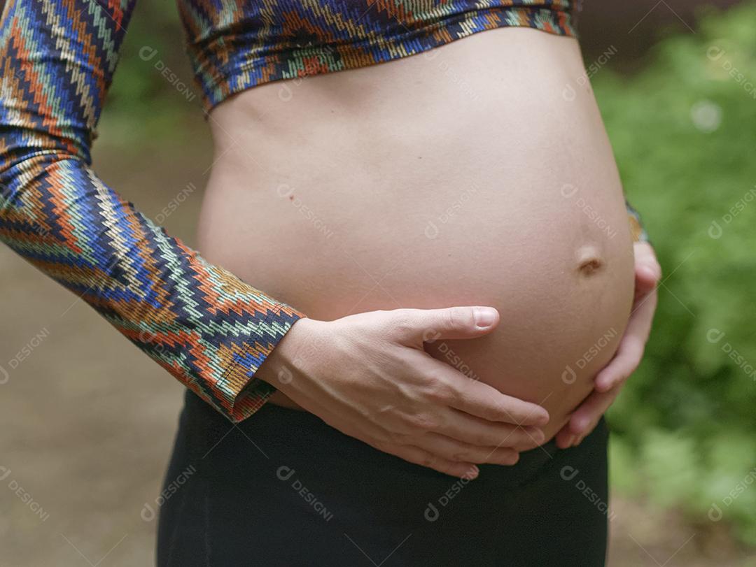 Mulher jovem moderna grávida tocando sua barriga ao ar livre.