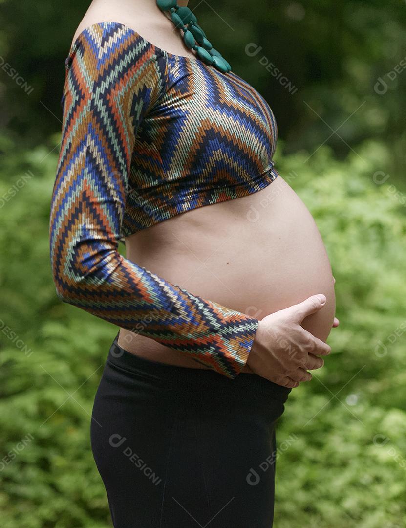 Mulher jovem moderna grávida tocando sua barriga ao ar livre.