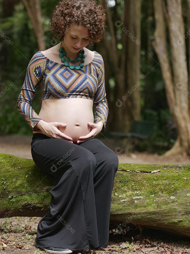 Mulher jovem moderna grávida tocando sua barriga ao ar livre.