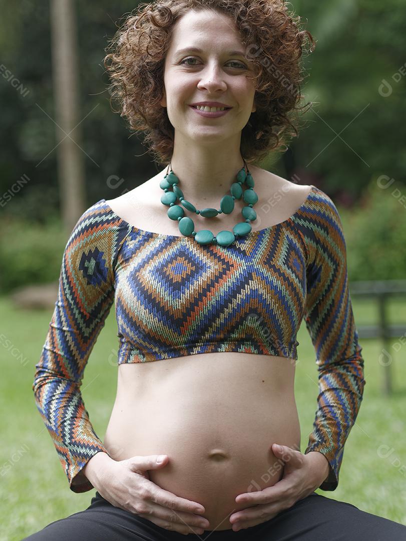 Mulher jovem moderna grávida tocando sua barriga ao ar livre.