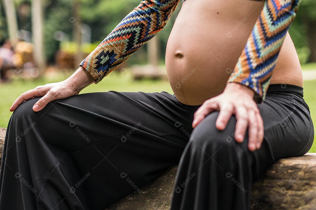 Perto da jovem grávida moderna tocando sua barriga ao ar livre.