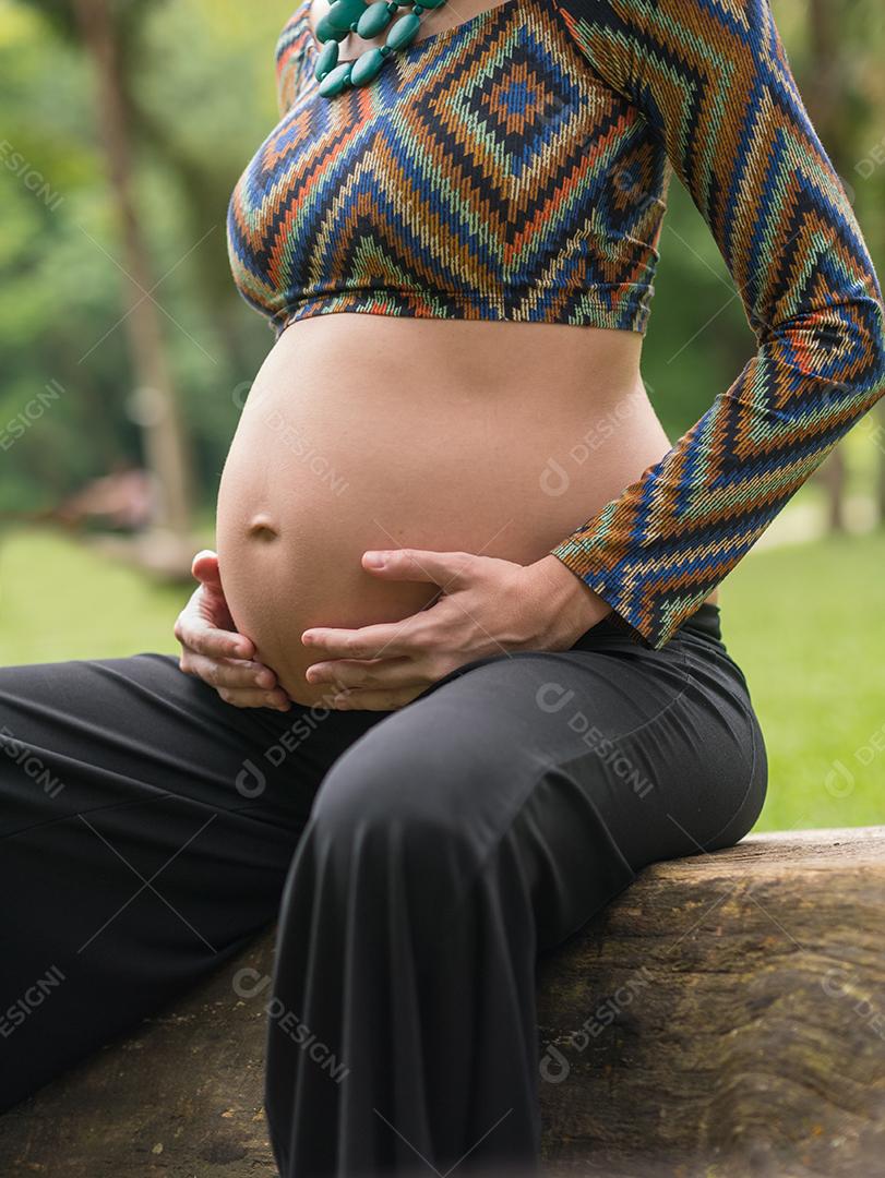 Mulher jovem moderna grávida tocando sua barriga ao ar livre.