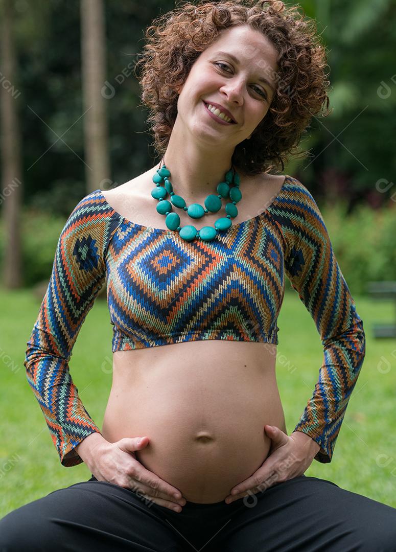Mulher jovem moderna grávida tocando sua barriga ao ar livre.